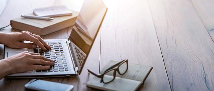 Hands typing on laptop surrounded by notebooks